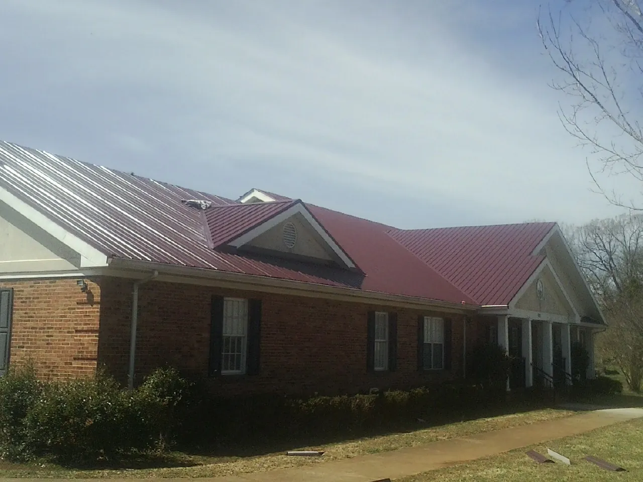 Red metal roof with gabled entries on a long brick building, from a Hail Damage Roof Repair job in Tower City