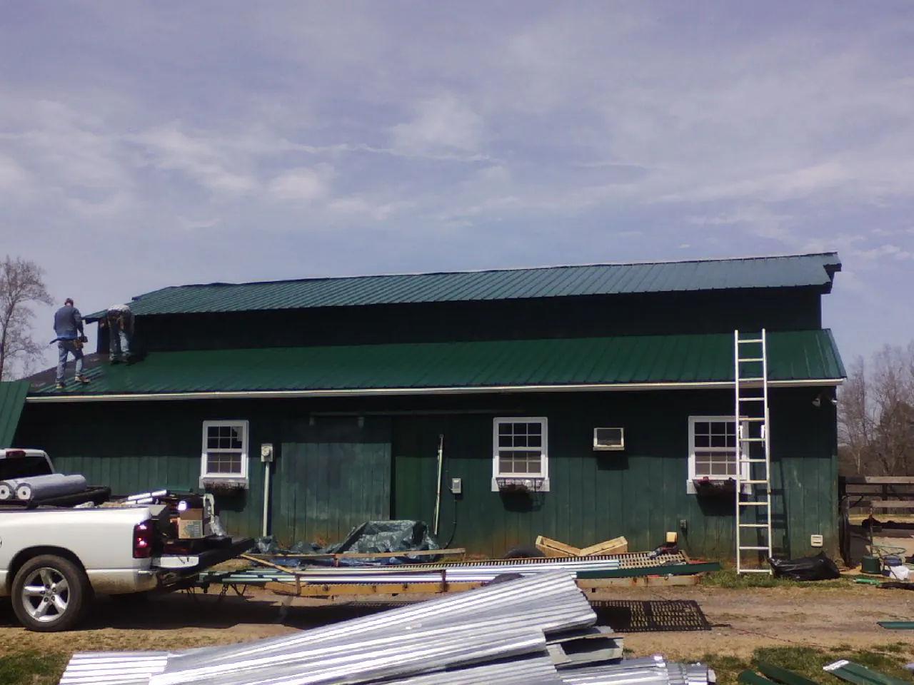 Crew installing green metal roofing on a large green barn in Tower City