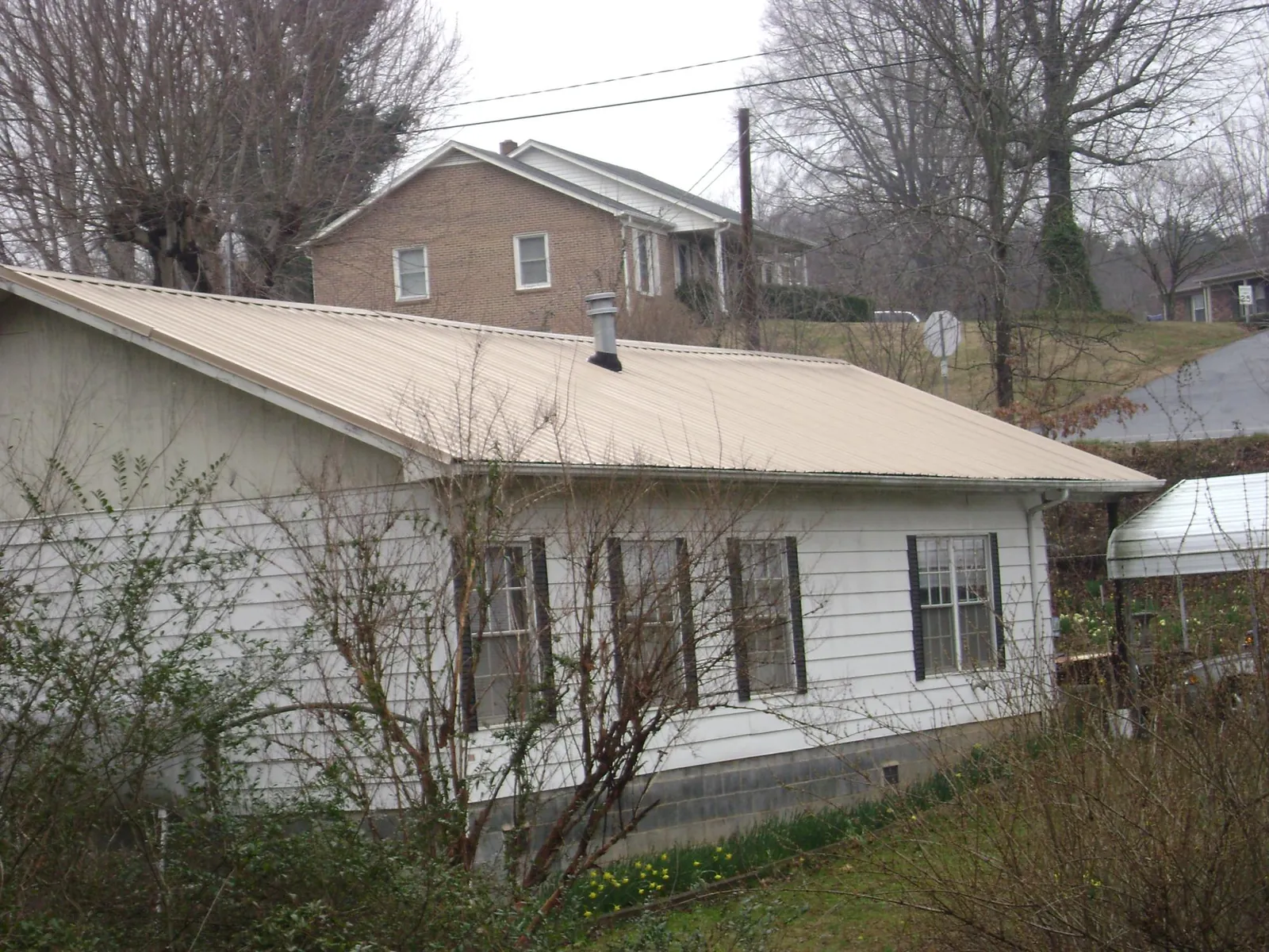 Tan metal roof on a white sided house set into a hillside — Commercial Roofing by Roofing Brothers in Tower City